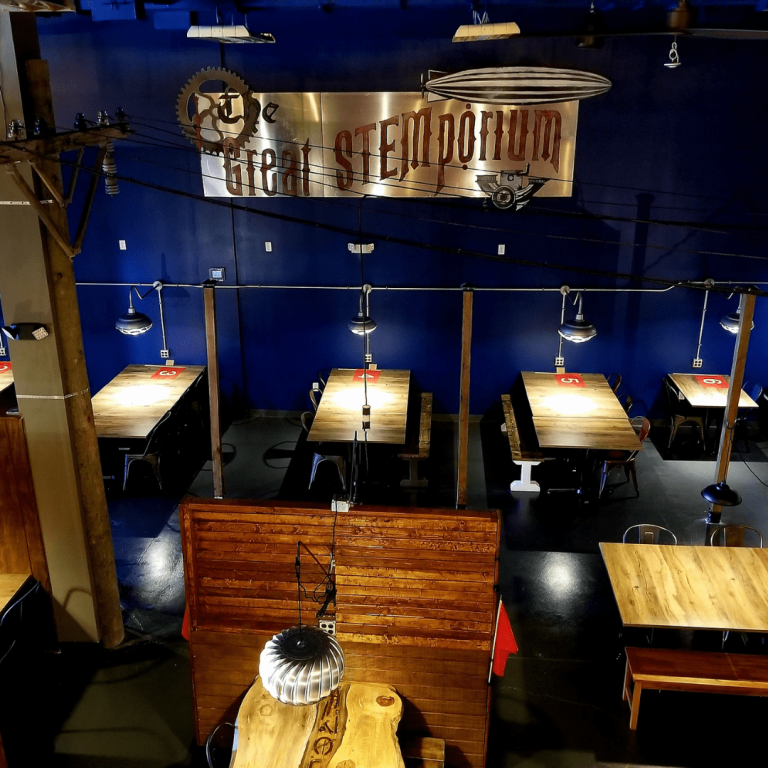 A space with tables and chairs with the logo of the Great STEMporium on a wall