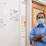 A man in a light blue shirt wearing a face mask