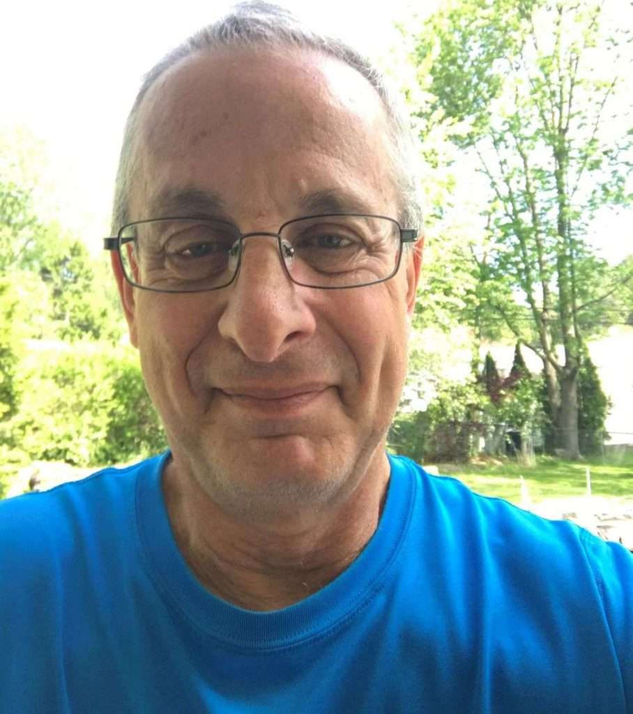 A headshot of a man in a blue shirt wearing glasses