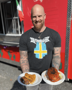 A man holding plates of tacos and sandwich in both hands.