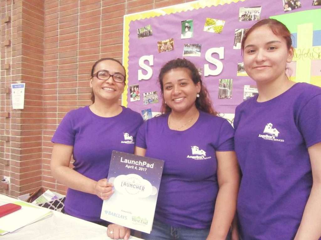 Three women in purple shirts holding Angelica's Cleaning Service promotional materials