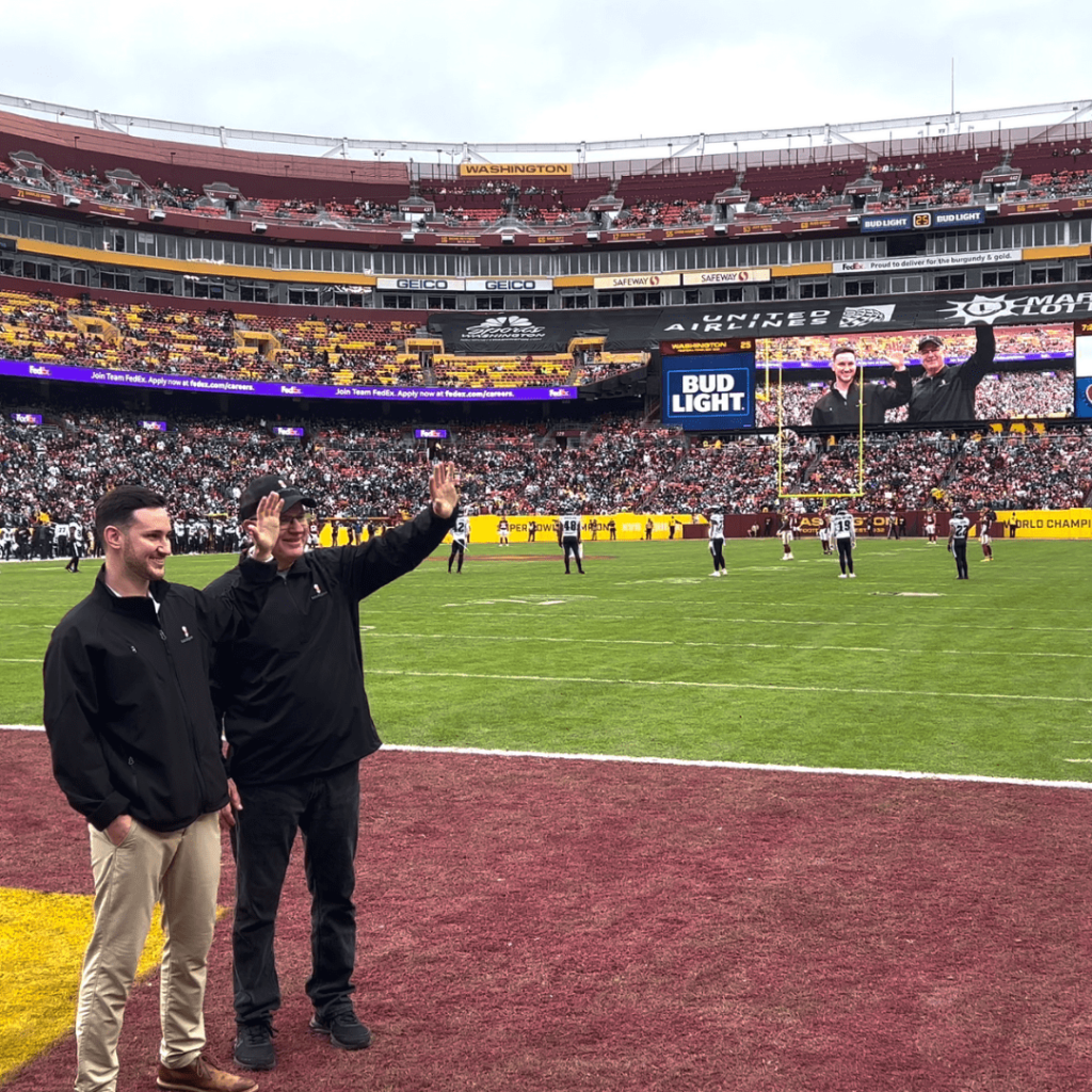 Two men on a football field with a crowd in the stands.