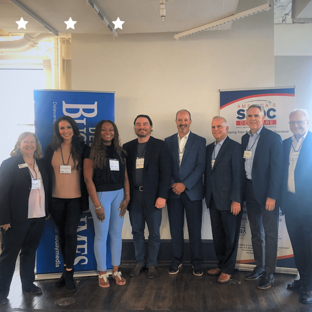Eight people in professional attire standing in front of a flier at an event