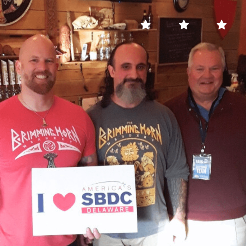 Three men in a pub holding "I love SBDC" sign
