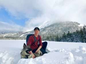 A white man sitting in the snow with a dog.