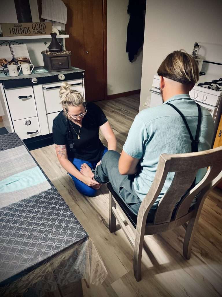 A woman giving a foot massage to another person in a chair.