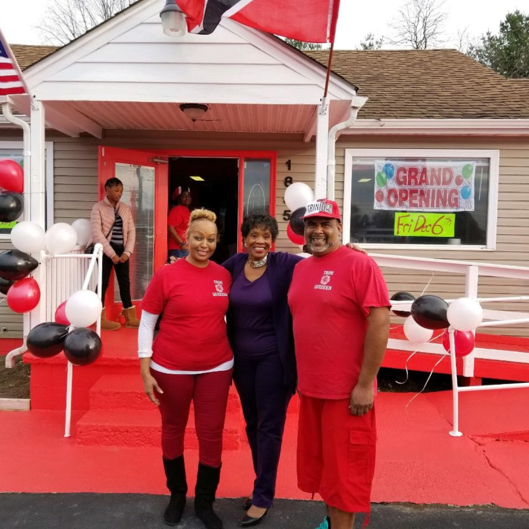Three people standing in front of a red shop at the grand opening