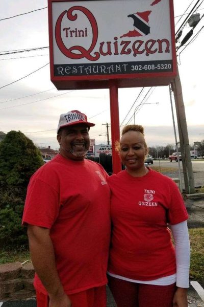 A man and a woman standing in front of a sign wearing red shirts