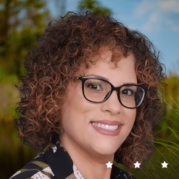 A headshot of a woman with curly hair wearing glasses