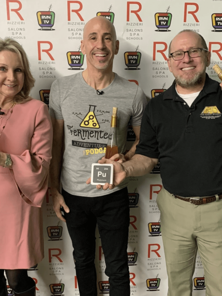 Three people standing behind a poster holding liquid alchemy beverages