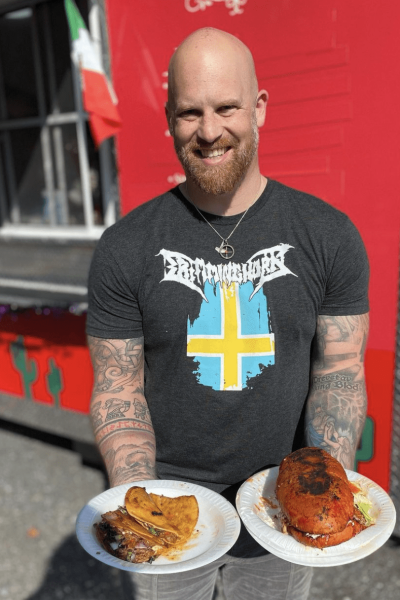 A man holding plates of tacos and sandwich in both hands.
